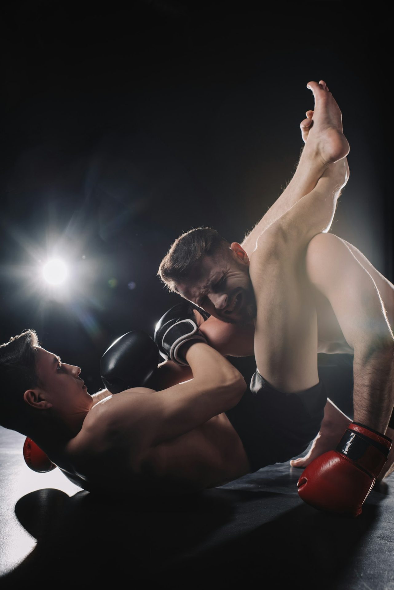 strong shirtless mma fighter doing painful joint lock with legs to another sportsman on floor